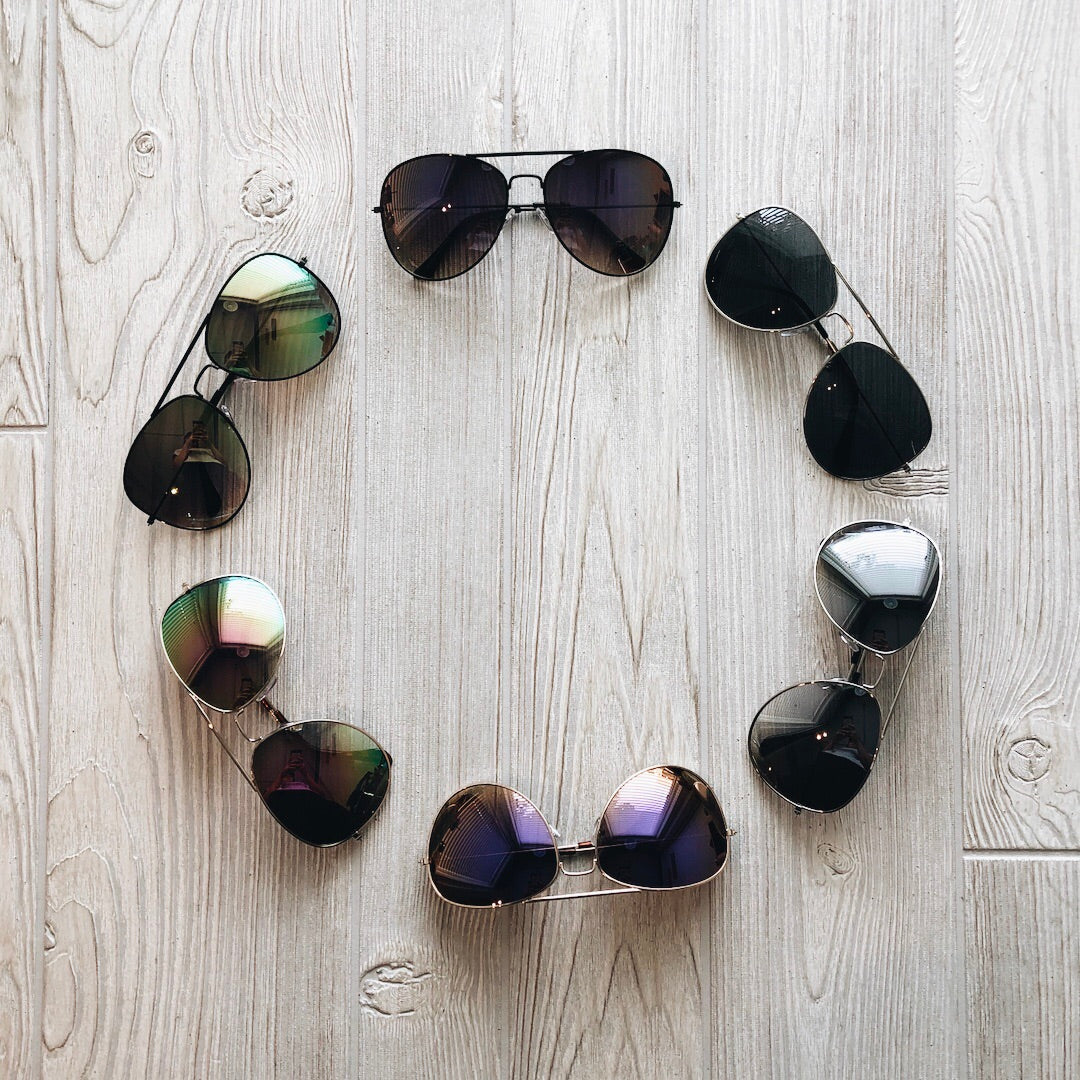 Six pairs of XL Avi Sunnies • Adult arranged in a circle on a light wooden floor, each pair facing outward to display different colorways.