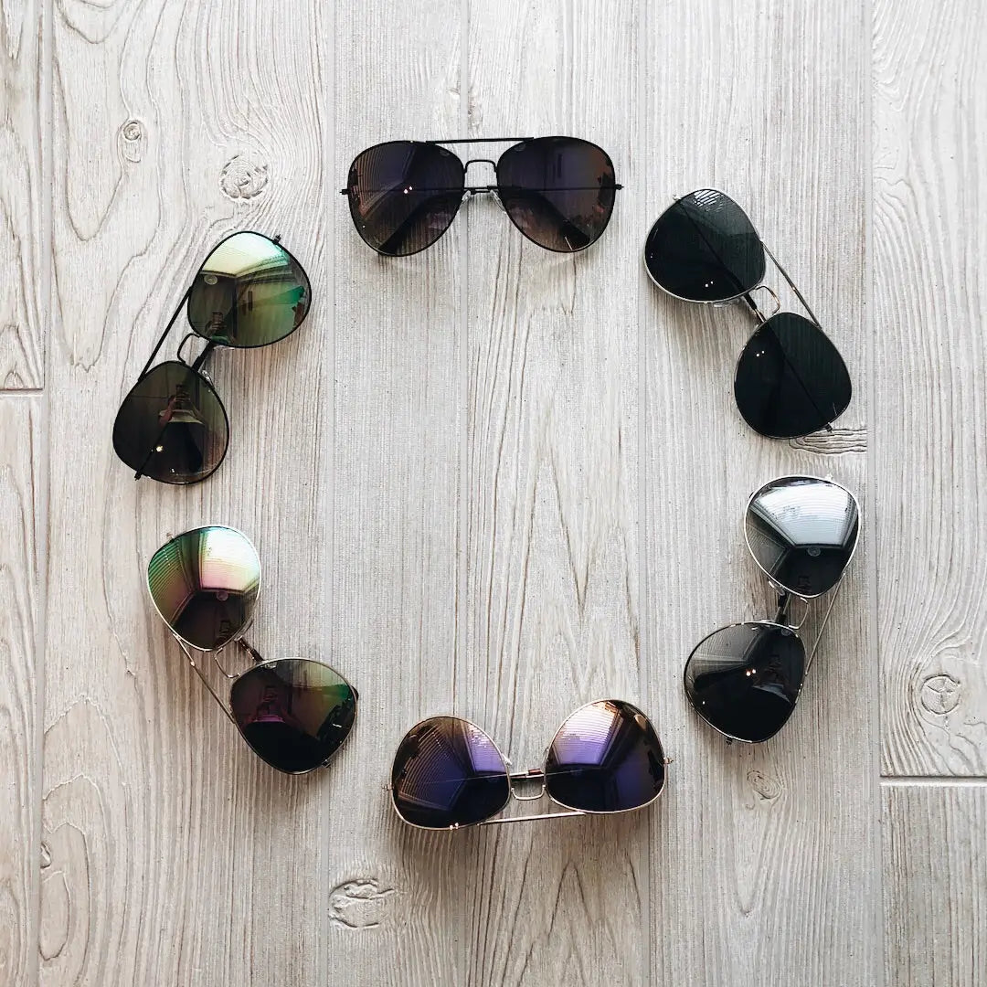 Six pairs of XL Avi Sunnies • Adult arranged in a circle on a light wooden floor, each pair facing outward to display different colorways.