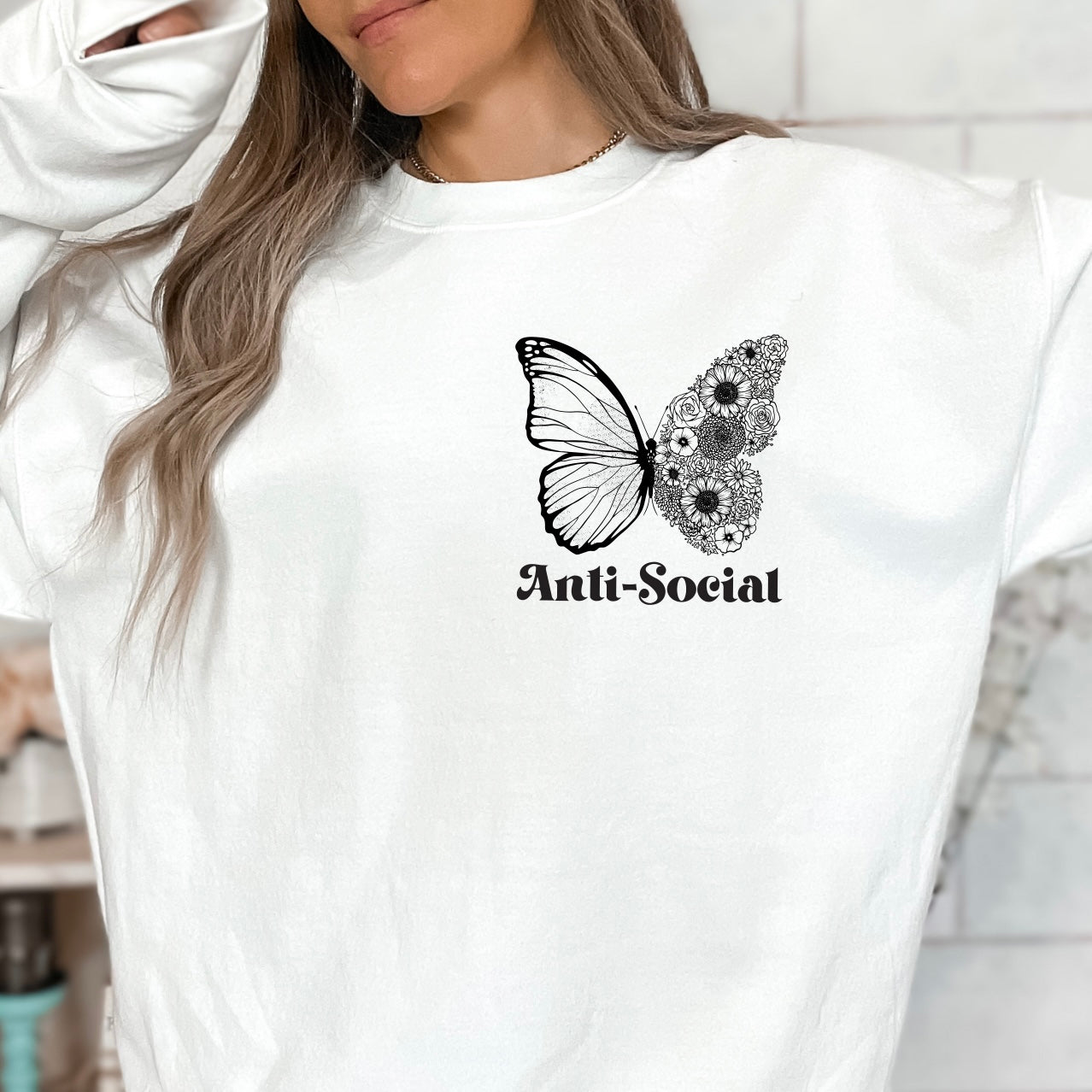 A woman wears the Anti-Social • White Sweatshirt, a comfy cotton/polyester pullover featuring a black butterfly and floral graphic with “Anti-Social” text—perfect for anti-social butterfly moms.