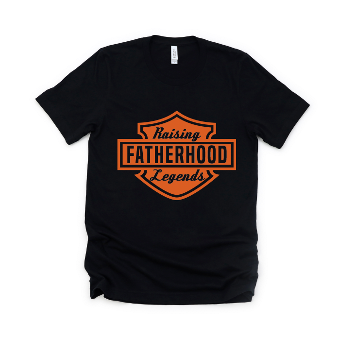 The Raising Legends • Black Tee is a soft ring-spun cotton crew neck in black, featuring an orange badge with Raising Fatherhood Legends in bold and script fonts. Unisex sizing ensures a comfortable fit for everyone.