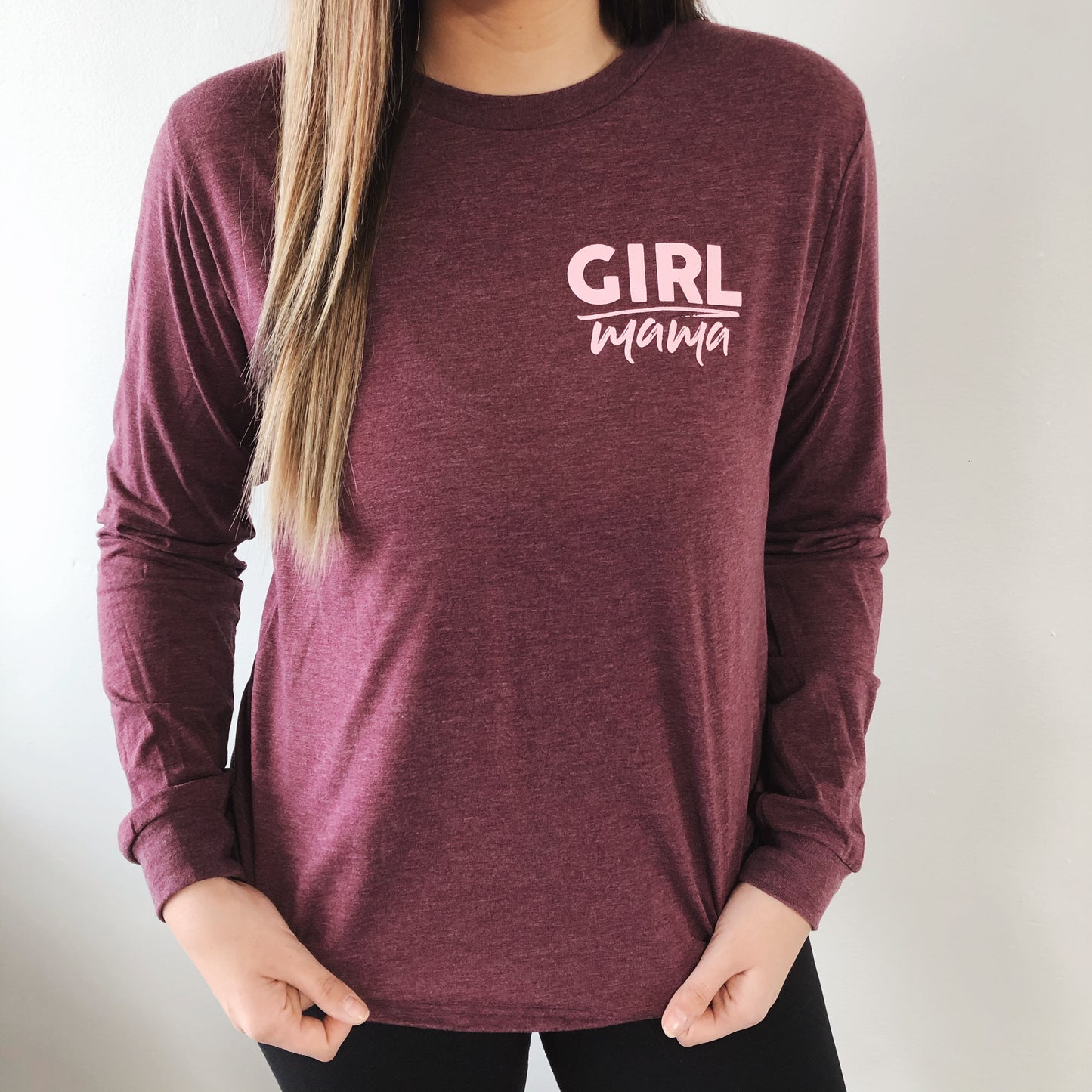 A woman wears the Girl Mama • Heathered Maroon Long Sleeve, a unisex shirt with GIRL mama in white on the upper left chest, standing against a plain light background.