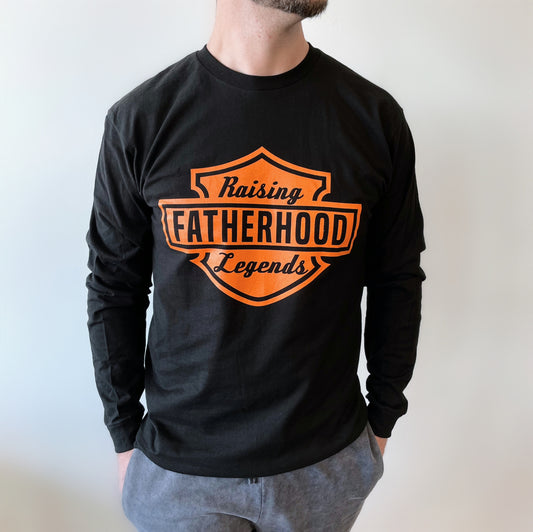 A man wearing the Legends • Dad Long Sleeve—black, unisex, made of soft ring-spun cotton with an orange shield-shaped Raising Fatherhood Legends logo—stands against a plain white background.