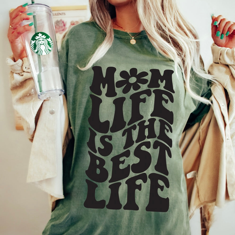 Wearing the Groovy Mom Life • Comfort Colors shirt featuring bold black MOM LIFE IS THE BEST LIFE text, a person holds a Starbucks cup and displays painted green nails.