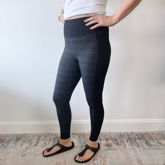 A person wears Cuffed Leggings • 6191 in black and gray, paired with a white shirt and black sandals, standing on a patterned rug against a white wall. Their hands rest on their hips, head out of frame.
