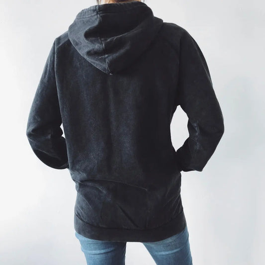 A person stands with their back to the camera, wearing the MAMA VIBES • Rocker Hoodie in black vintage wash and blue jeans against a plain white background.