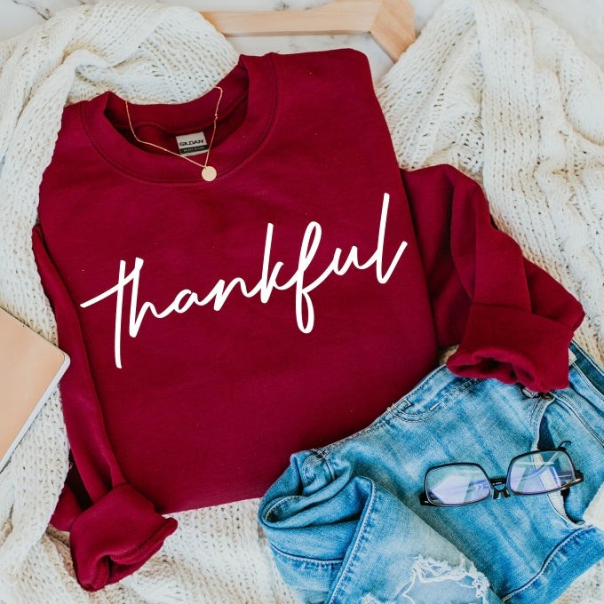 The Thankful • Cardinal Pullover is a maroon unisex sweatshirt with Thankful in white script—cozy for cooler weather and perfect paired with denim or layered for comfort.