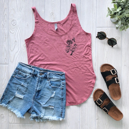 A flat lay features the Hummingbird • Dark Mauve Tank, distressed denim shorts, brown double-strap sandals, round sunglasses, and a small green plant on light wood—perfect for relaxed summer womens style.