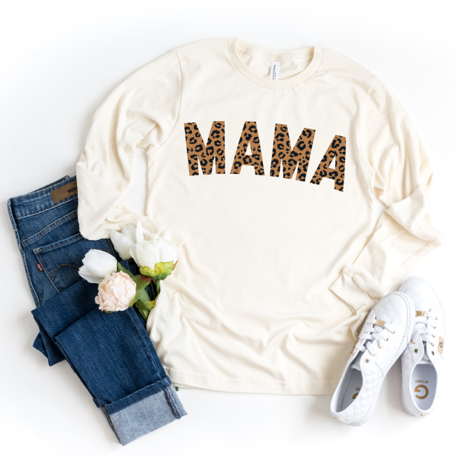 Flat lay of the MAMA Cheetah • Long Sleeved tee in cream with cheetah print, styled with blue jeans, white sneakers, and white flowers on a white background. Comes in unisex sizing for all.