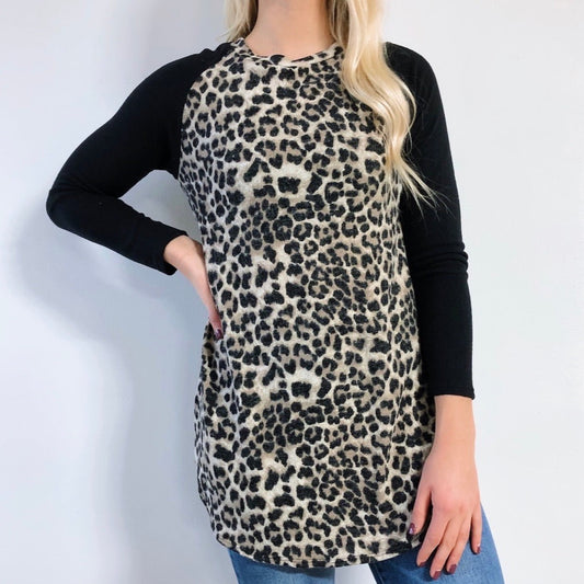 A woman wears the Long Sleeve Cheetah Raglan (size small) featuring black sleeves and a leopard print body, paired with blue jeans, standing against a plain white background.