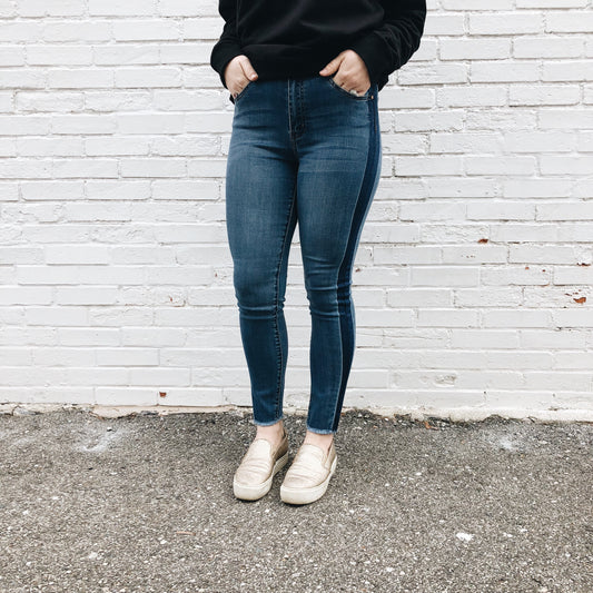 Standing against a white brick wall, the person wears Alie Jeggings SIZE 0 & 3 that fit true to size, a black sweatshirt, and beige slip-on shoes. The photo is cropped at the shoulders, keeping their face out of frame.