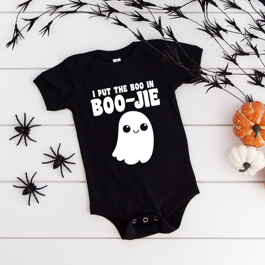 The Boo in BOO-JIE • Bodysuit is a black baby bodysuit featuring the phrase I put the boo in BOO-JIE with a cute ghost, accented by black spiders, faux branches, and small pumpkins on a white background.