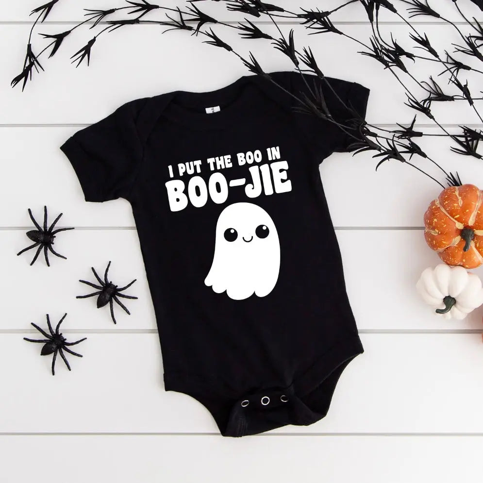 The Boo in BOO-JIE • Bodysuit is a black baby bodysuit featuring the phrase I put the boo in BOO-JIE with a cute ghost, accented by black spiders, faux branches, and small pumpkins on a white background.
