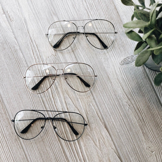 Three pairs of Alex • Blue Light Glasses • More Colors! with metal frames are displayed on a light wooden surface next to a small green potted plant, perfect for reducing eye strain.