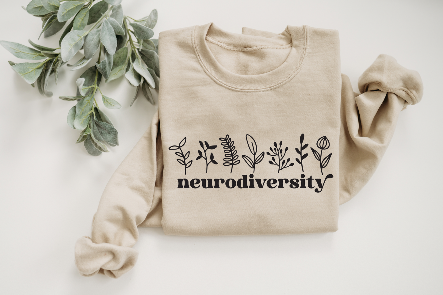 The Neurodiversity • Sand Pullover is a cozy, beige fleece-lined sweatshirt with “neurodiversity” in bold black letters and simple botanical designs, crafted from a preshrunk cotton/polyester blend.