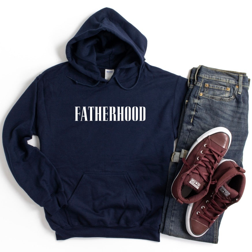 The Fatherhood • Navy Hoodie in a standard fit, featuring FATHERHOOD in white, is styled with blue jeans and maroon sneakers on a white backdrop.