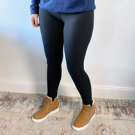 Person wearing a blue top, Favorite Leggings in black (buttery soft), and brown ankle boots with side zippers, standing on a multicolored rug against a white wall.