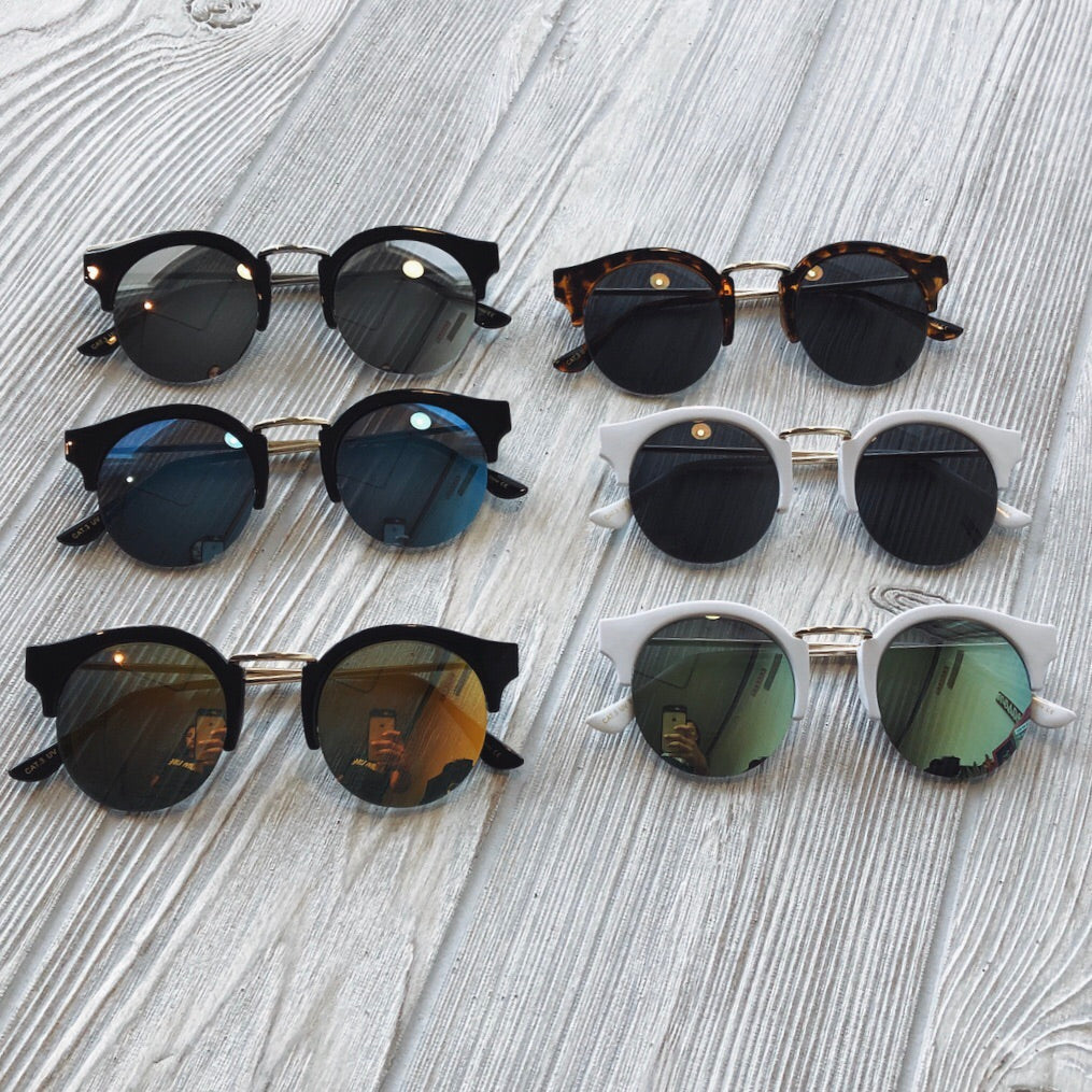Six pairs of Ray • Adult Sunglasses with round lenses and frames in black, tortoiseshell, and white are neatly displayed on a light gray wooden surface. All offer UV400 protection. Final Sale.