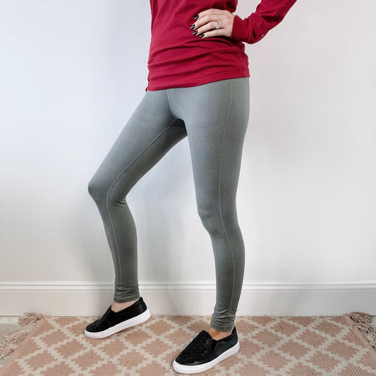 A person stands indoors on a patterned rug, wearing a long-sleeve red shirt and the Basic Sage Leggings • 6168 with a yoga style waistband, paired with black slip-on shoes. The photo is cropped from the shoulders down.