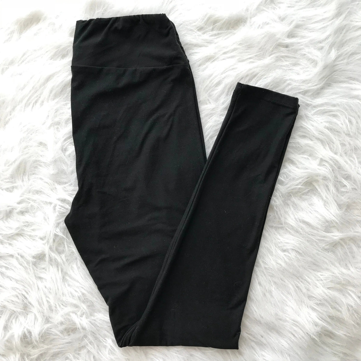A pair of Wide-Waist Leggings in plain black, made from super-soft brushed jersey, shown laid flat on a fluffy white surface. Available in more colors!.