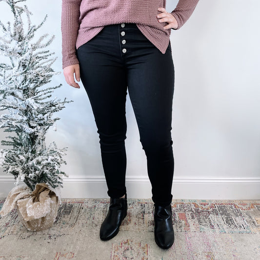A person in a mauve sweater, Phalesha Jeggings SIZE 0 & 1 (black, true to fit spandex), and black boots stands indoors beside a small snow-dusted artificial tree wrapped in burlap.