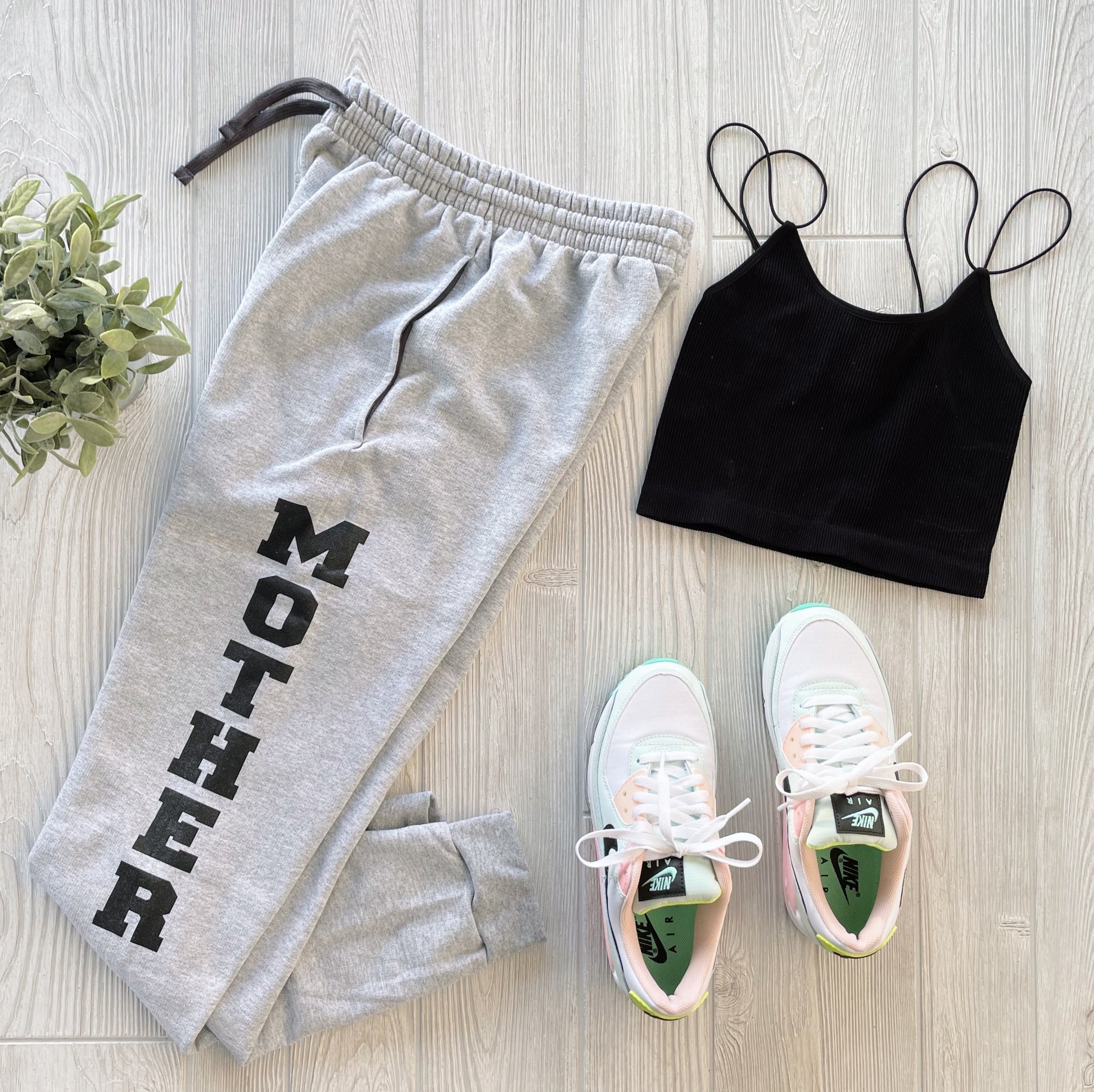 MOTHER • Joggers paired with a black spaghetti strap crop top, white pastel-accented sneakers, and a small green potted plant on a light wood floor create the perfect loungewear look.