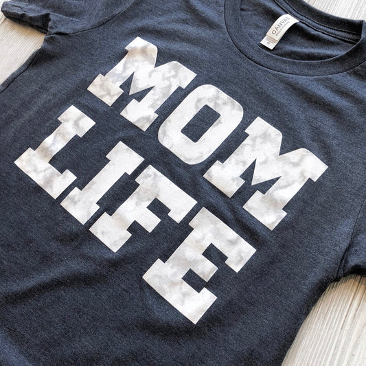 A unisex navy marble print tee featuring MOM LIFE in bold white letters across the front.