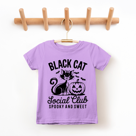 The Black Cat Social Club • Kids Tee is a lavender children’s T-shirt made of soft combed ring-spun cotton. It features a black cat, jack-o’-lantern, bats, and “Black Cat Social Club Spooky and Sweet” in bold black text.