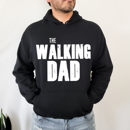 A man stands with hands in his pockets, wearing The Walking Dad • Black Hoodie—crafted from pill-resistant fleece and featuring bold white THE WALKING DAD lettering on the front.