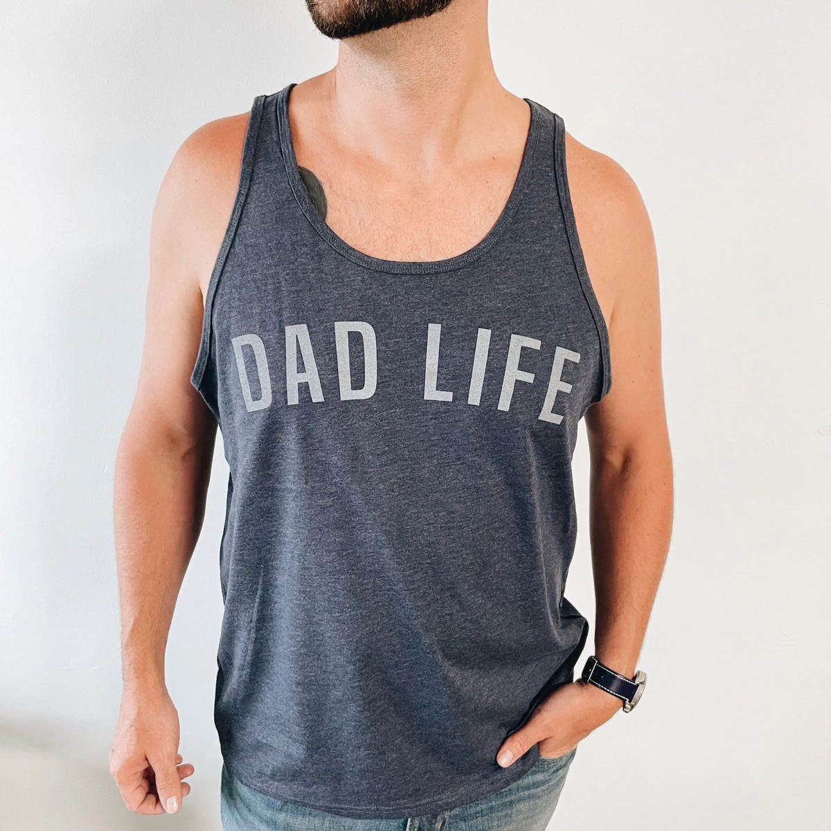 A man stands against a white background wearing a navy DAD LIFE tank top, featuring bold white lettering across the chest.